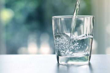 Close up pouring purified fresh drink water from the bottle on table in living room